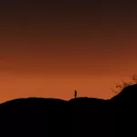 Silhouette eines Menschen auf Felsen beim Sonnenuntergang an der Spitzkoppe, Namibia