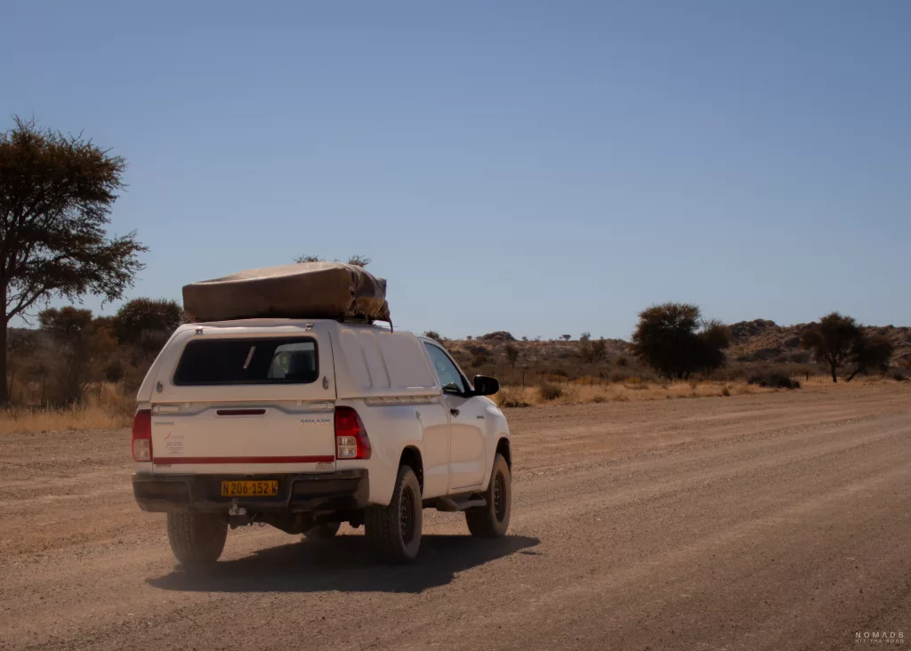 Weißer Pickup mit Dachzelt von hinten auf einer Schotterstraße auf einer Namibia Rundreise