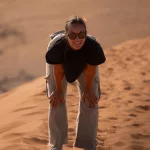 Frau in schwarzem Tshirt läuft eine Düne hoch und macht gerade eine Pause