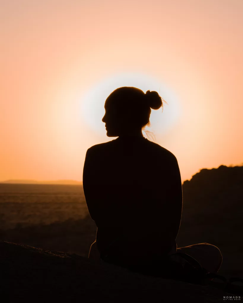 Frau von hinten sitzend auf einem Felsen vor einem Sonnenuntergang in Spitzekoppe
