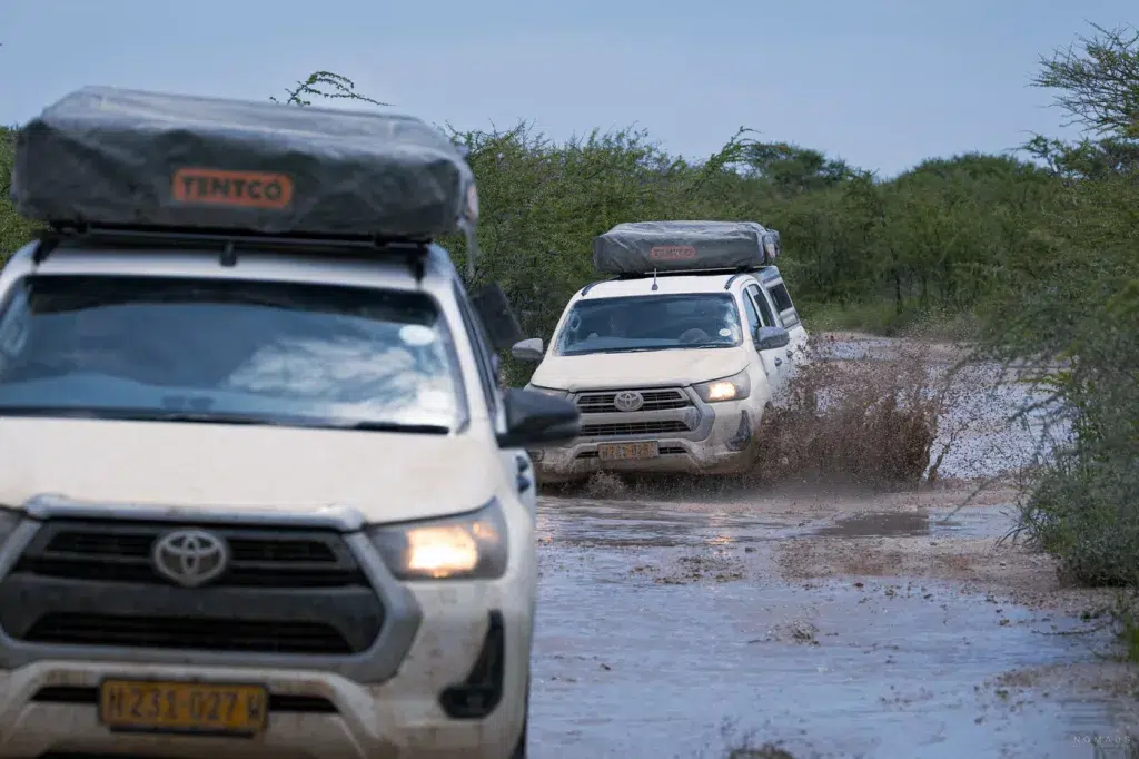 Kolonne von Offroad-Fahrzeugen durchfährt schlammige Pisten im Etosha Nationalpark während der Regenzeit.