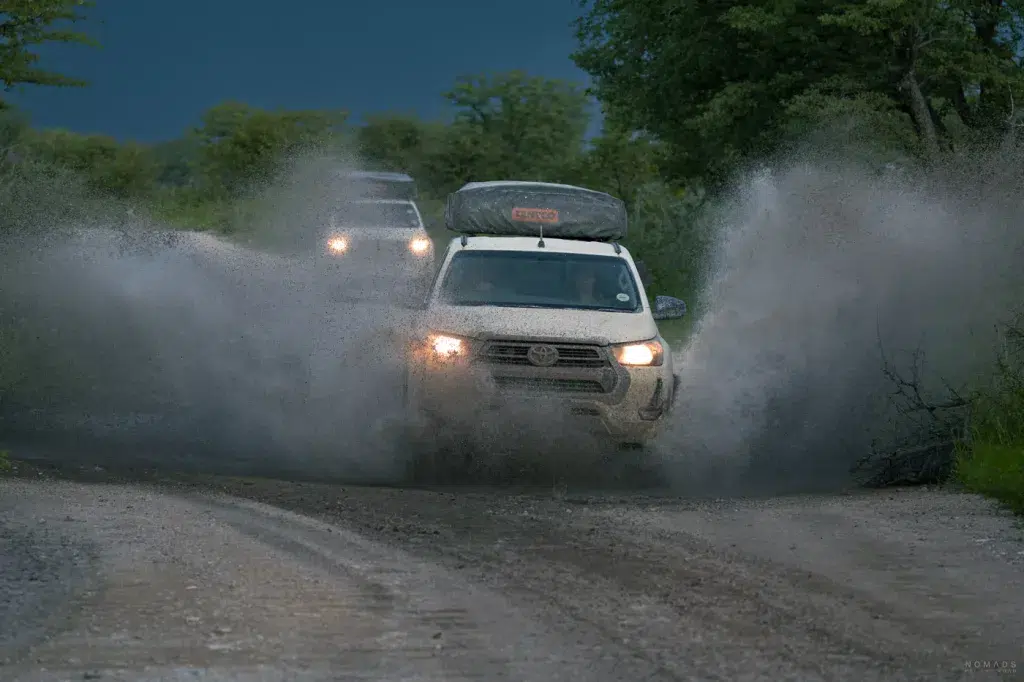 4x4 Fahrzeug fährt durch eine große Wasserpfütze im Etosha Nationalpark nach starkem Regen.
