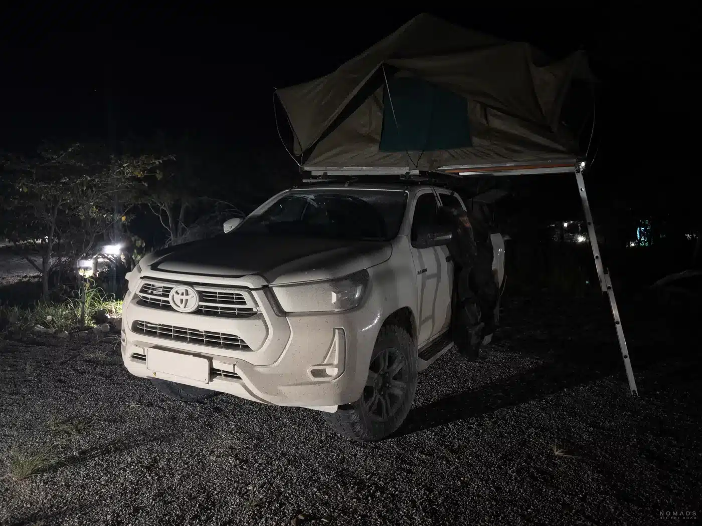 Toyota Hilux mit aufgebautem Dachzelt auf einem Stellplatz der Etosha Village Campsite bei Nacht, beleuchtet von Umgebungslichtern.