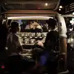 Produkte werden aus einem Auto verkauft, wo Menschen davor sitzen