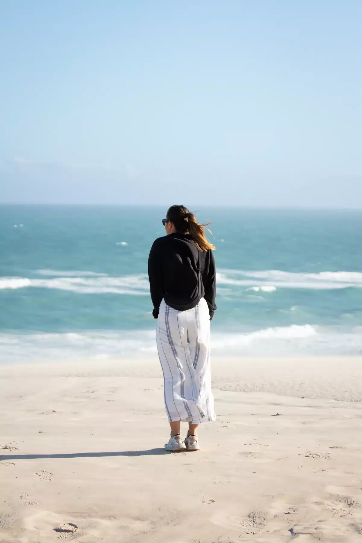 Frau steht am Strand mit Blick auf Meer