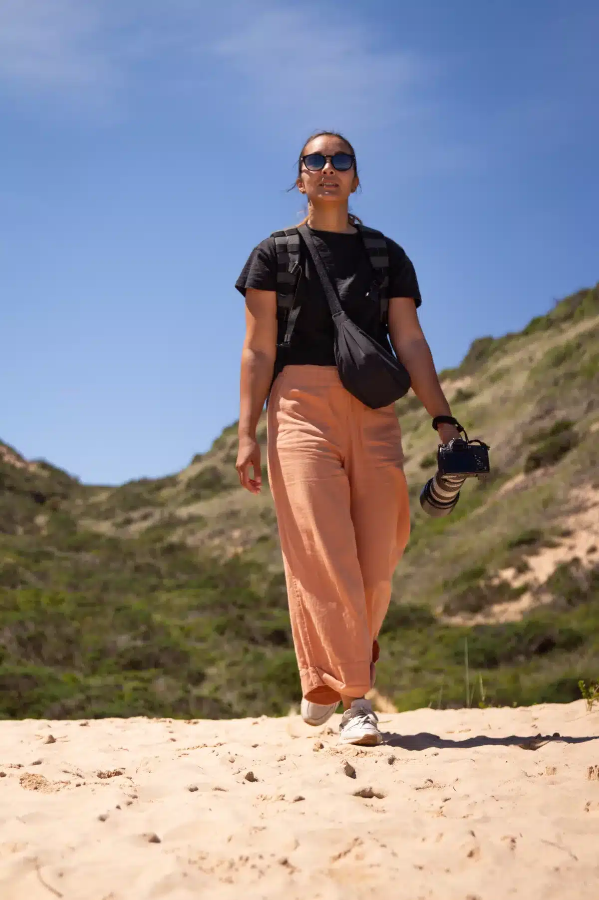 Frau in orangefarbener Hose und Kamera in der Hand auf dem Robberg Hiking Trail in Plettenberg Bay