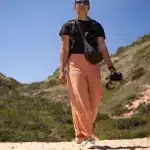 Frau in orangefarbener Hose und Kamera in der Hand auf dem Robberg Hiking Trail in Plettenberg Bay