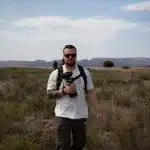 Mann läuft mit einem Tele-Objektiv durch das hohe Gras des Mountain Zebra National Parks