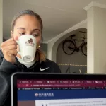Frau trinkt in einem Café aus einer Tasse während ein Laptop augeklappt vor ihr steht