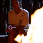 Frau sitzt im Dunkeln am Lagerfeuer für Braai