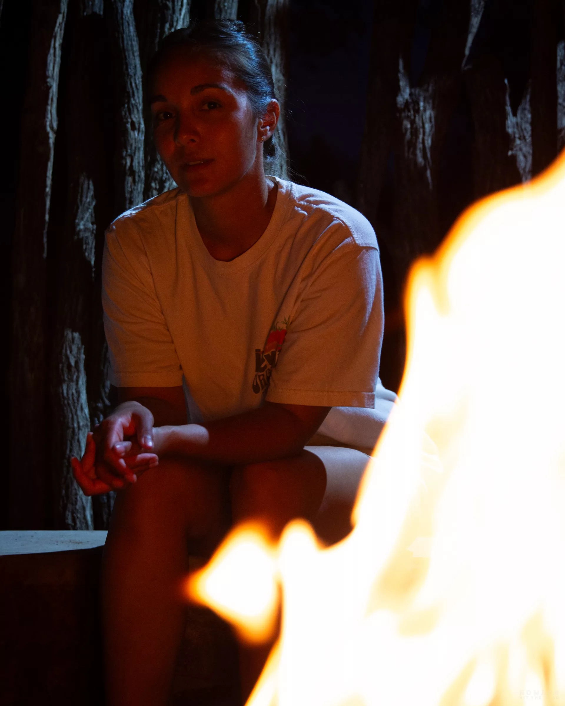 Frau sitzt im Dunkeln am Lagerfeuer für Braai