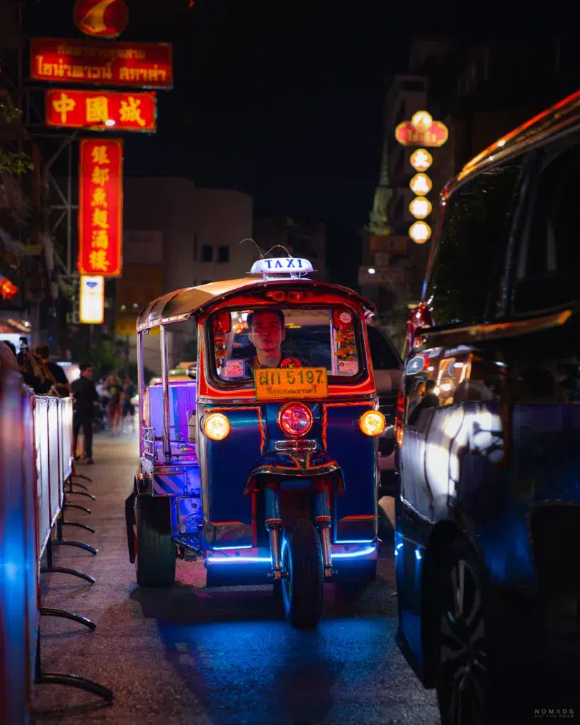 ein Tuk-Tuk fährt nachts durch die beleuchteten Straßen von Chinatown Bangkok.