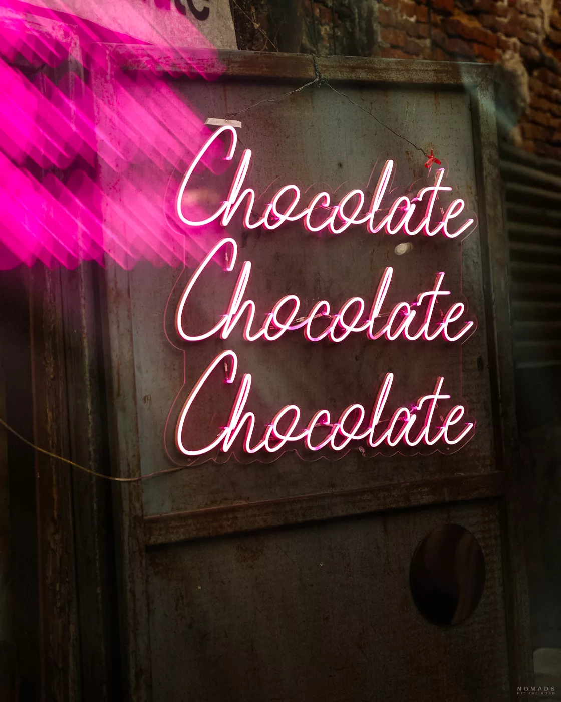 Ein pinkes Neonschild mit der Aufschrift 'Chocolate' in Schreibschrift an einer Hauswand in Talat Noi, Bangkok.