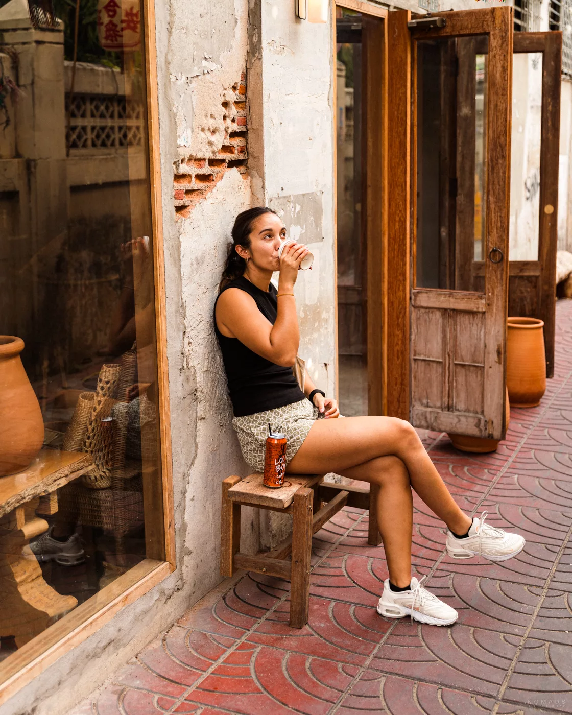 Eine junge Frau sitzt entspannt auf einer Bank und trinkt einen Kaffee in einem Café auf der Song Wat Road in Bangkok.
