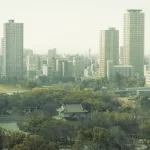 Modern meets Tradition, traditionelle Häuser im Grünen treffen auf moderne Hochhäuser im Hintergrund.
