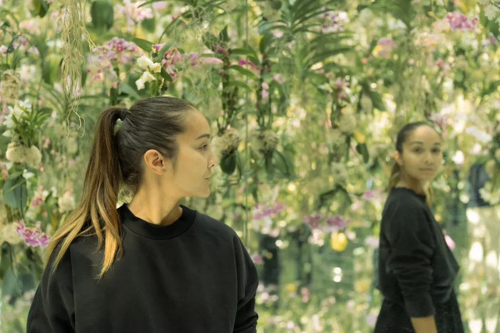 Frau und ihre Spiegelung inmitten von Blumen, die von der Decke hängen