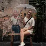 Frau mit Regenschirm sitzt vor Street Art in der Gasse Kwai Chai Hong in Chinatown Kuala Lumpur