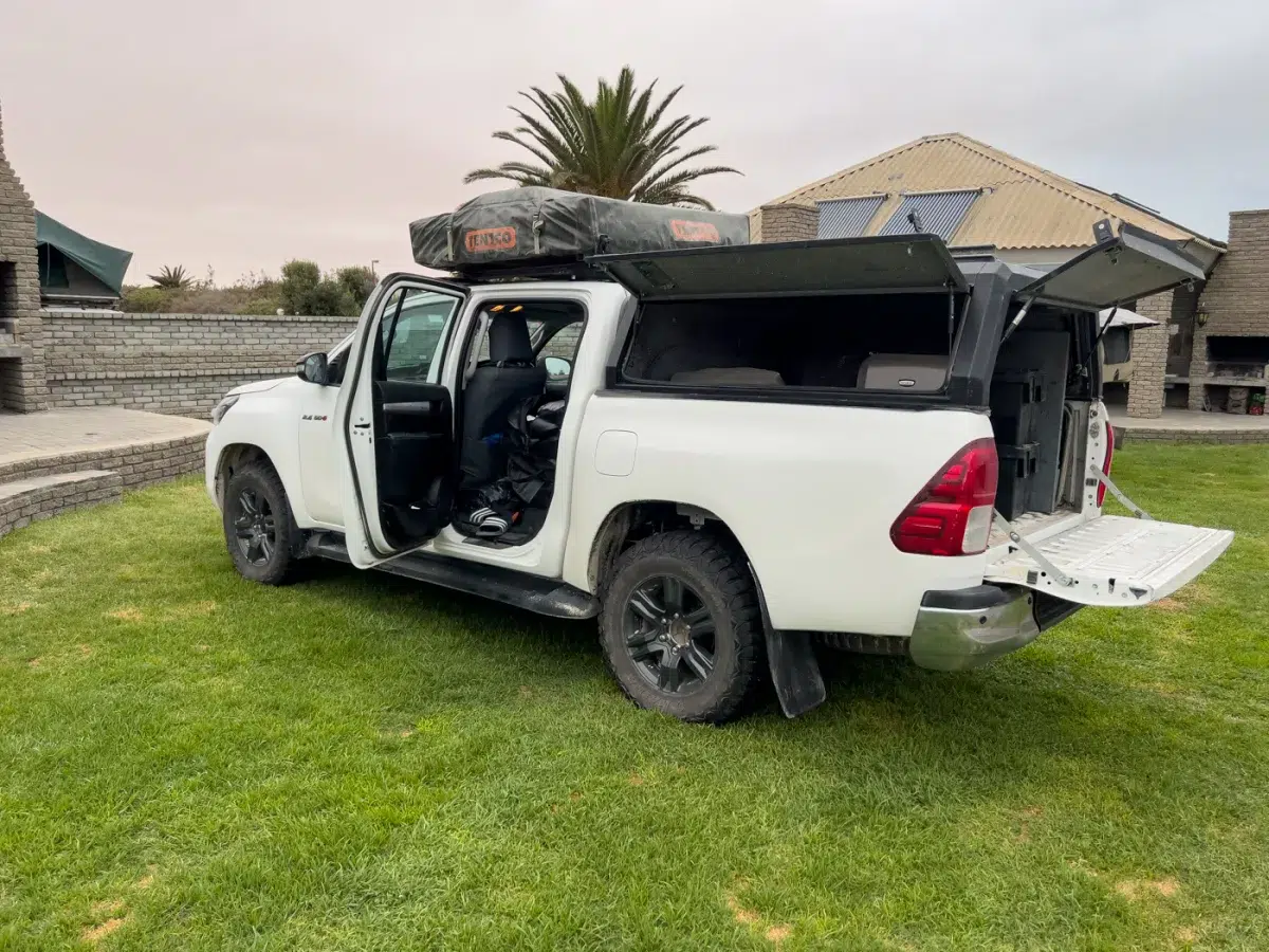 Pick-up Mietwagen mit geöffnetem Heckdeckel, zeigt die beladene Ladefläche mit Koffern, Campingausrüstung und Stauboxen.