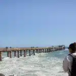 Frau mit Rucksack schaut sich den Jetty Pier vom Ufer aus an