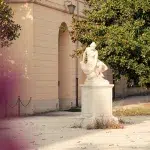 Statue von Frau vor einem Baum und Gebäude