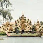 Ein goldener Palastbau am Wasser in der Ancient City, Bangkok, umgeben von üppigem Grün.