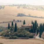 Podere Belvedere, Bauernhof mit Zypressen umgeben von golden wirkenden Feldern in der Toskana