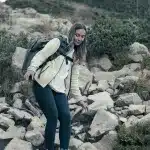 Wanderin in Outdoor-Ausrüstung steigt vorsichtig über steinigen Pfad im Pirin-Gebirge, umgeben von alpiner Vegetation.