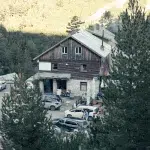 Berghütte Wichren, umgeben von Nadelbäumen im Pirin-Gebirge, mit geparkten Autos und Wanderern auf dem Vorplatz.
