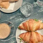 Frühstücksteller mit Croissants, gefüllt mit Schinken und Käse, neben frisch gebrühtem Kaffee, serviert auf einem rustikalen Holztisch.