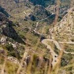 Kurvenreiche Straße nach Sa Calobra auf Mallorca, die sich durch dramatische Felslandschaften und steile Berghänge schlängelt, mit Autos und einem Bus, die die Serpentinen hinabfahren.