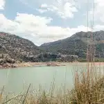 Aussicht auf einen ruhigen See, umgeben von Hügeln und bewaldeten Bergen unter einem blauen Himmel mit weißen Wolken auf der MA10 durch das Tramuntana Gebirge