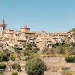 Panoramaansicht des Dorfes Valldemossa auf Mallorca mit seinen charakteristischen Steinhäusern und der Kirche vor einem klaren blauen Himmel.
