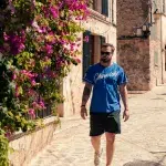 Ein Mann spaziert durch eine blumengeschmückte Gasse in Valldemossa, Mallorca, vorbei an leuchtenden Bougainvillea und traditionellen Steinhäusern.