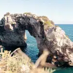 Der natürliche Felsbogen „Es Pontas“ nahe Santanyi auf Mallorca, der majestätisch aus dem blauen Meer herausragt und von klarem Himmel umgeben ist.