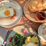Frühstück in Albanien – traditionelles Petulla mit Honig, Avocado-Toast und Spiegelei auf Brot.