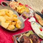 Traditionelles albanisches Mittagessen mit gegrillten Qofte, Kartoffeln und Salat, serviert auf einer rustikalen Tafel.