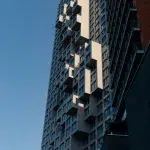 Ein modernes Hochhaus mit einer auffälligen, geometrischen Fassade, bei der einige Würfelformen hervortreten, im Kontrast zu einem klaren blauen Himmel.