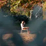 Eine ruhige Szene in Tiranas Grünanlagen: Eine Frau sitzt entspannt unter den herbstlichen Bäumen, durch eine kreative Perspektive eingefangen.