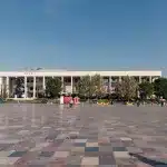 Opernhaus am Skanderbeg-Platz in Tirana, eingerahmt von Grünflächen und einer modernen Skyline, unter strahlendem Sonnenschein.