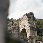 Nahaufnahme von antiken Ruinen in Berat, Albanien, mit einem erhaltenen Steinbogen und grünem Hintergrund.