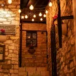 Eine beleuchtete Treppe führt zu einem charmanten Innenhof in Berat, Albanien, umgeben von Steinwänden und dekorativen Lichtern.