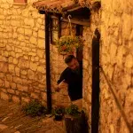 Ein Mann vor dem Restaurant Beratino in einer engen, gepflasterten Gasse in Berat, Albanien, bei stimmungsvollem Abendlicht.