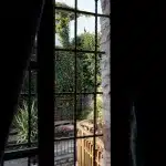 Blick durch ein Fenster auf einen begrünten Innenhof in Gjirokastër – Ein einladender Kontrast zwischen Steinarchitektur und lebendigem Grün.