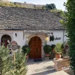 Eingang zum Hotel Kekezi in Gjirokastër – Traditionelles Gebäude mit Steinplatte-Dach und einladender Dekoration aus Pflanzen.
