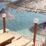 Schattige Liegestühle mit Strohdächern und Blick auf das kristallklare Wasser der Riviera.