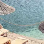 Liegestühle und Strohdächer direkt am türkisfarbenen Wasser der albanischen Küste – perfekte Entspannung am Meer.