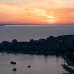Atemberaubender Sonnenuntergang über der Küste, mit Blick auf die Stadt und Segelboote, die in der Bucht ruhen.