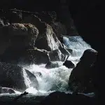 Nahaufnahme des sprudelnden Wassers in der Partnachklamm, das sich kraftvoll seinen Weg über große Felsen bahnt – ein Moment, der die rohe Energie der Natur einfängt.
