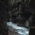 Die schmale Partnachklamm mit ihrem rauschenden Fluss, umgeben von steilen, moosbewachsenen Felswänden. Ein Wanderer genießt den Ausblick von einem der sicheren Stege.