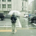 Frau steht mit Regenschirm an einem Zebrastreifen in Kyoto